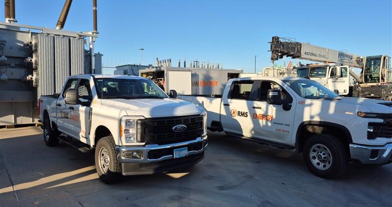 RMS Energy fleet vehicles and trailer parked at an electric power substation for specialized transformer service.