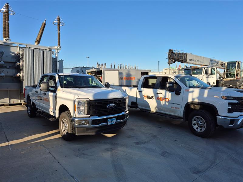 RMS Energy fleet vehicles and trailer parked at an electric power substation for specialized transformer service.